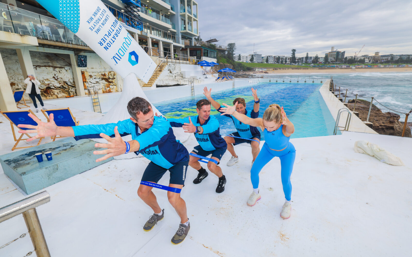 Body By Berner founder Bernadette Sukkar leads Bondi Lifeguards Deano, Joel, and Harries in poolside pilates at Liquid I.V. Bondi Icebergs Takeover A pilates class at the Bondi Icebergs infront of a giant LiquidIV structure.