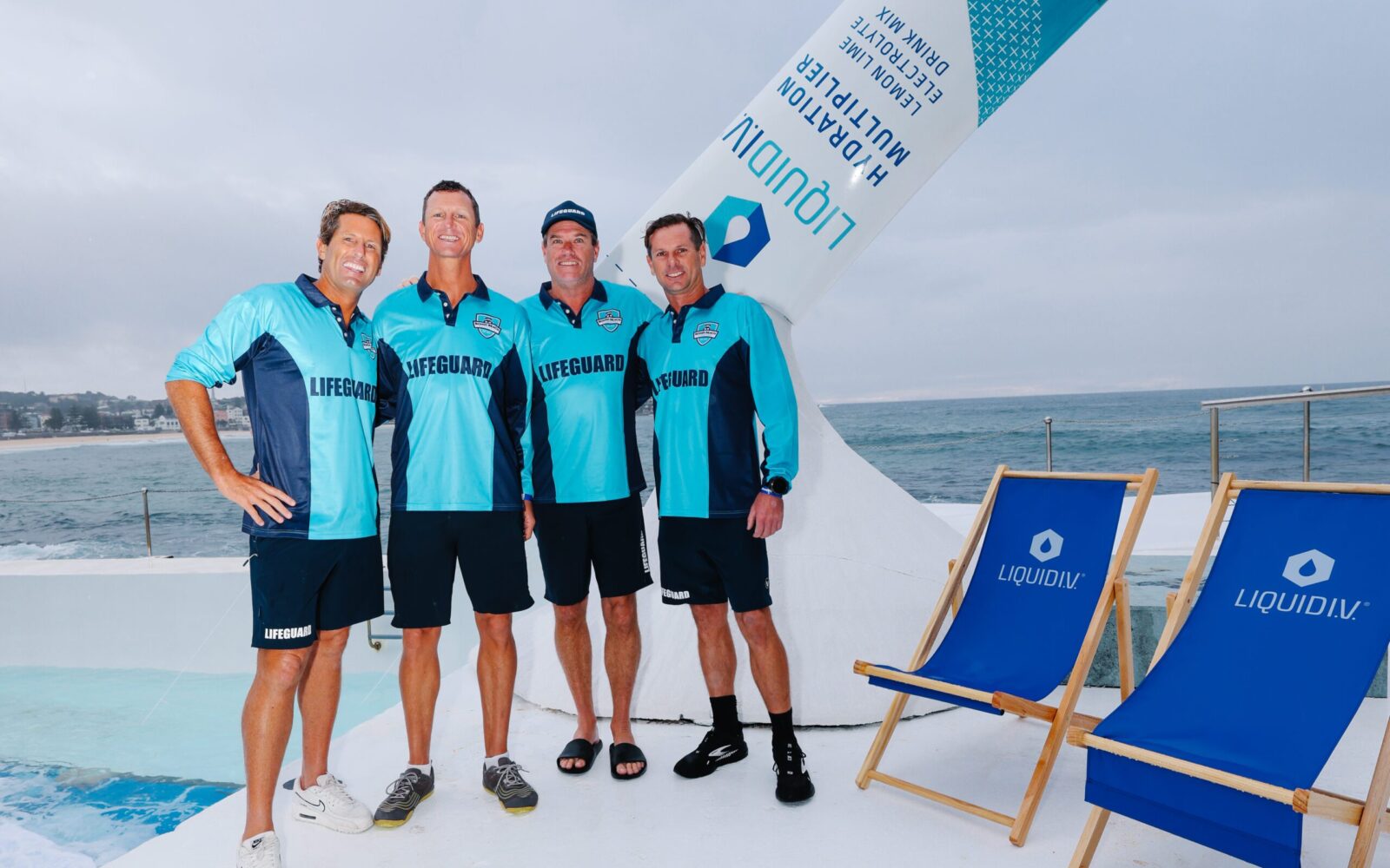 Bondi Lifeguards Harries, Deano, Hoppo and Joel at Liquid I.V. Bondi Icebergs Takeover (2) A group of Lifeguards standing infront of a giant LiquidIV structure and chairs.